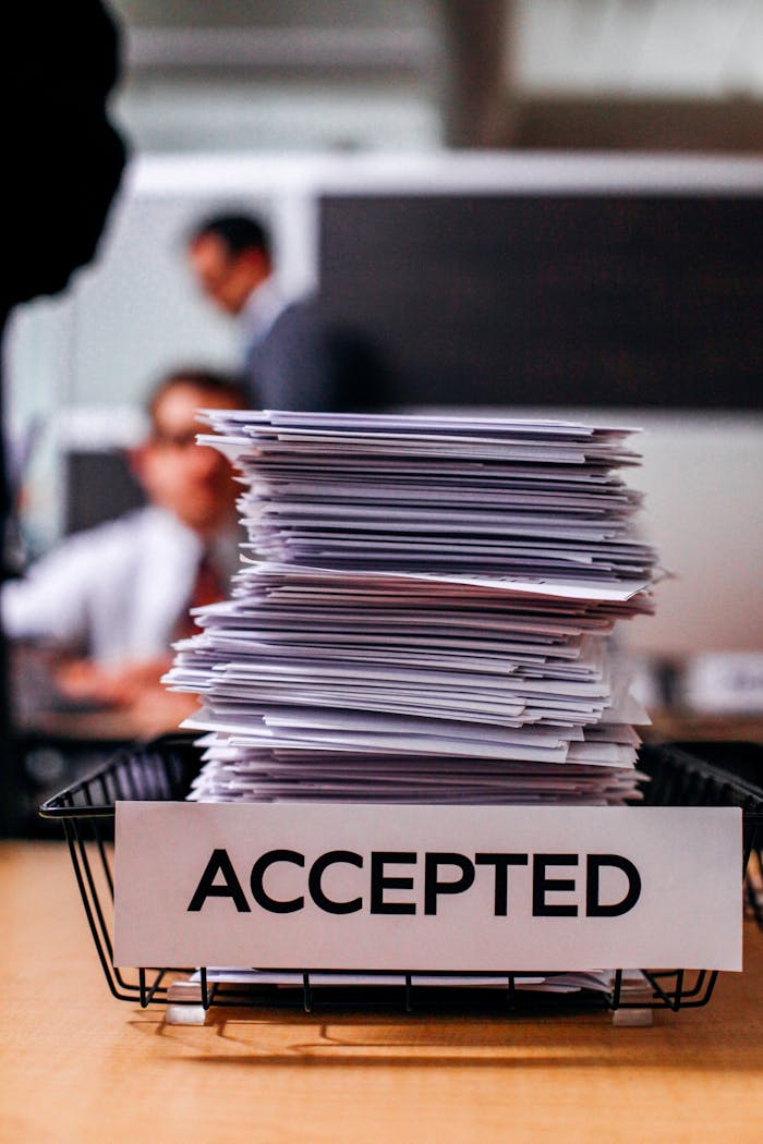 Pile of papers with Accepted label in a busy office setting, highlighting information management.