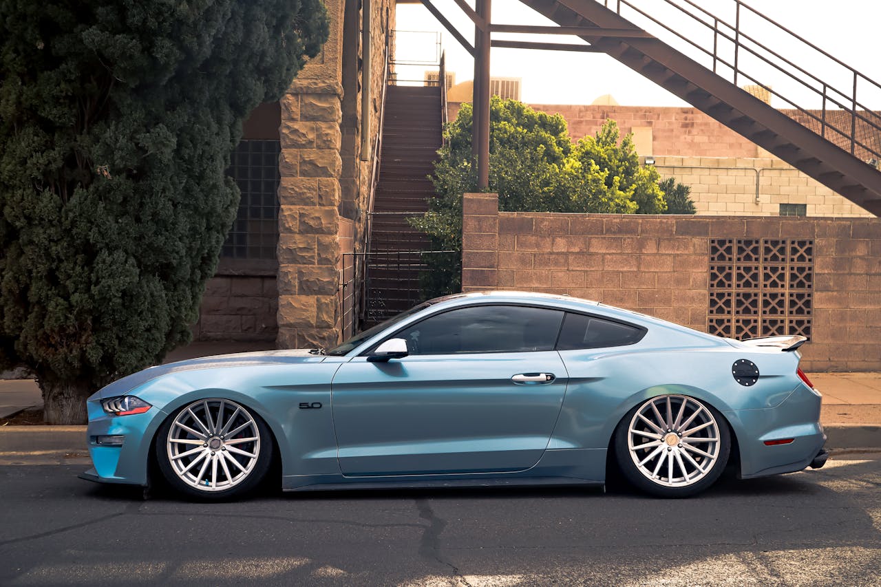 A sleek blue sports car parked beside an urban staircase on a sunny day.